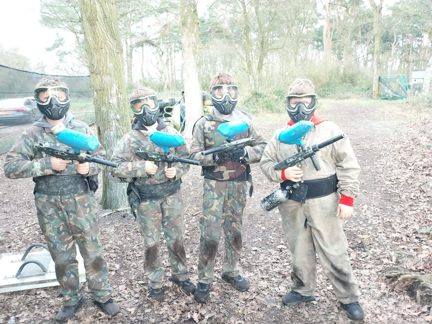 4 kids holding a paintball guns, happy, picture showing them in the woods with the full protective gear on