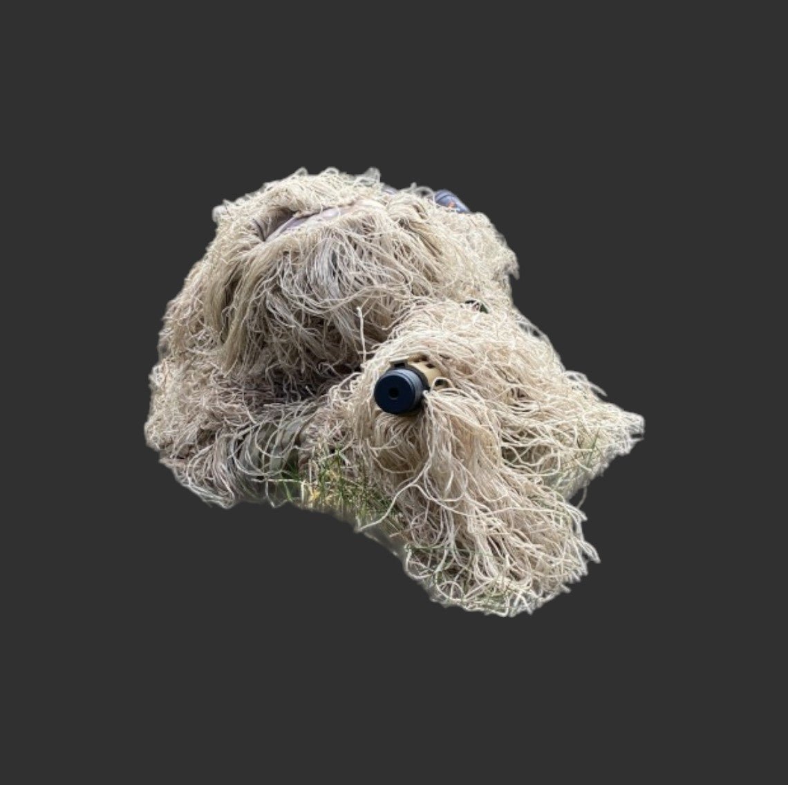 A tan dog with long, curly fur, partially covered by a BlasterMasters StealthGuard Gun Cover designed for camouflage, peeks out from under its coat with a black nose and dark eyes.